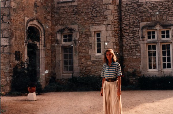 Femme en chemise rayée et jupe beige devant un château.ᴬᴵ