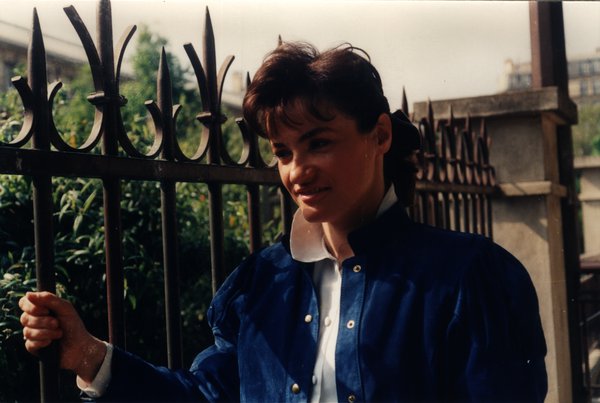 Femme en veste bleue près d'une grille en fer forgé.ᴬᴵ