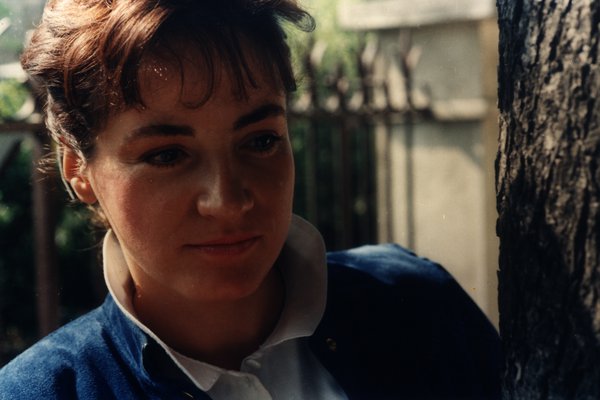 Portrait d'une femme en veste bleue appuyée contre un tronc d'arbre.ᴬᴵ