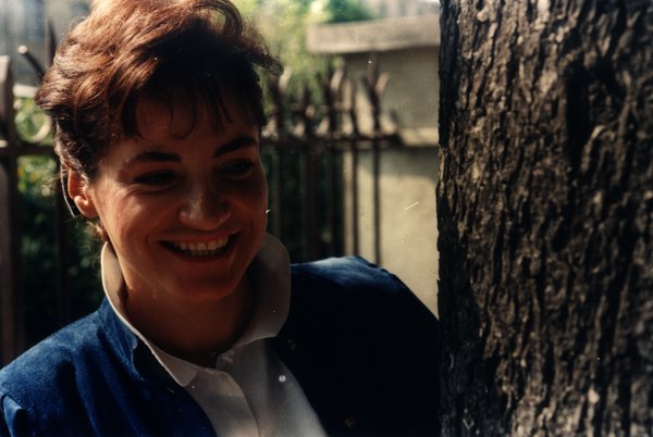 Portrait d'une femme en veste bleue souriant largement près d'un arbre.ᴬᴵ