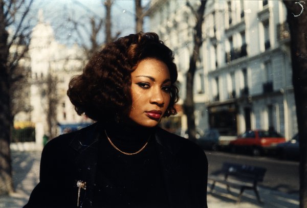 Femme aux cheveux bouclés dans une rue de Paris, dôme du Sacré-Cœur en arrière-plan.ᴬᴵ