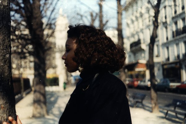Femme aux cheveux bouclés de profil près d'un arbre dans une rue de Paris.ᴬᴵ