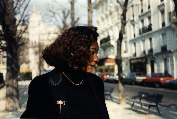 Femme aux cheveux bouclés avec une broche sur son manteau, dans une rue de Paris.ᴬᴵ