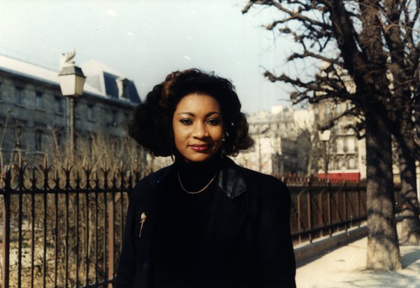 Portrait d'une femme aux cheveux bouclés près d'une grille en fer forgé.ᴬᴵ