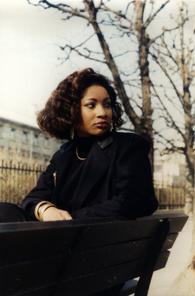 Femme aux cheveux bouclés assise sur un banc, arbres nus en arrière-plan.ᴬᴵ