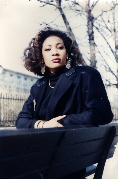 Femme aux cheveux bouclés assise sur un banc, regardant l'objectif.ᴬᴵ