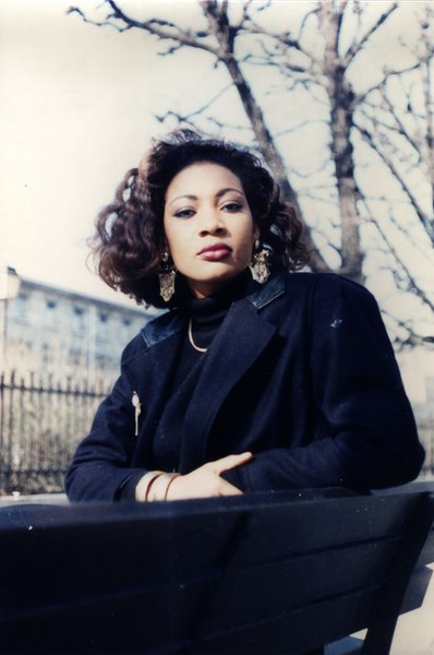 Femme aux cheveux bouclés assise sur un banc, bras croisés.ᴬᴵ