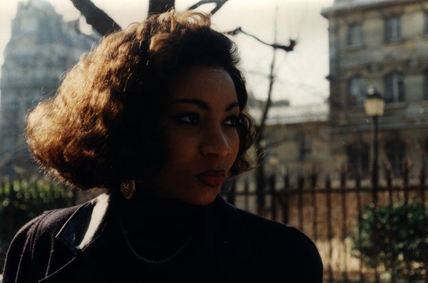 Portrait d'une femme aux cheveux bouclés regardant de côté, immeubles en arrière-plan.ᴬᴵ