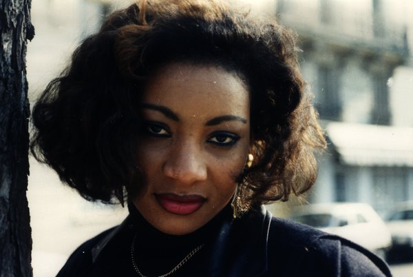 Portrait d'une femme aux cheveux bouclés regardant l'objectif, près d'un arbre.ᴬᴵ