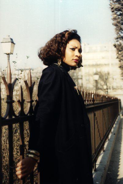 Femme en manteau noir près d'une grille en fer forgé et d'un lampadaire.ᴬᴵ
