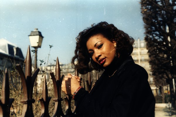 Femme aux cheveux bouclés jouant avec ses cheveux près d'une grille en fer.ᴬᴵ