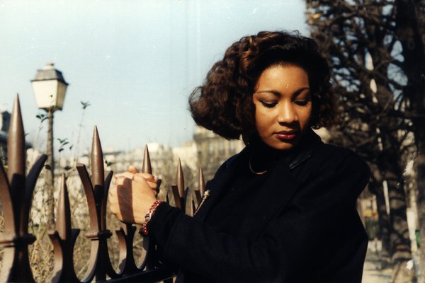 Femme aux cheveux bouclés regardant son poignet près d'une grille en fer.ᴬᴵ