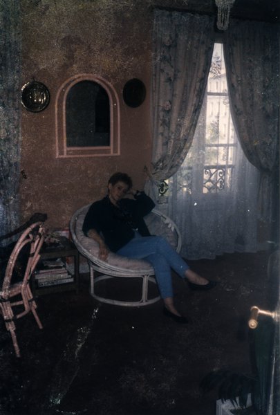 Femme assise dans un fauteuil en osier près d'une fenêtre à rideaux.ᴬᴵ
