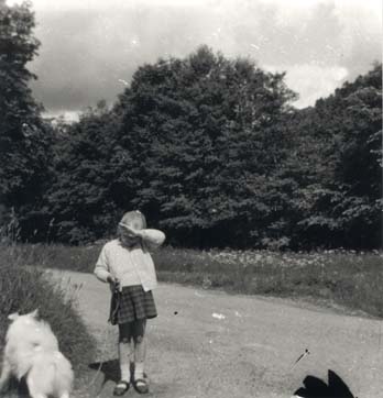 petite fille blonde en kilt avec un chien en laisse au bord d’une route à la campagne. Noir et blanc.