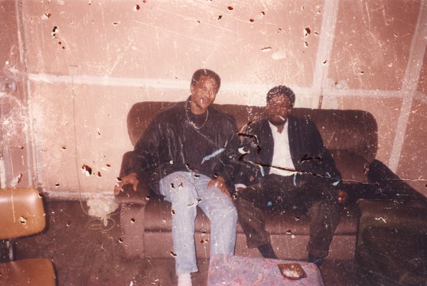 Deux hommes assis sur un canapé brun. Image avec rayures.
