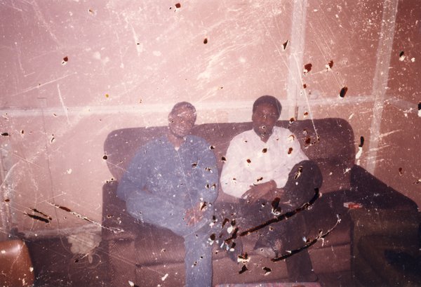 Deux hommes assis sur un canapé brun. Image avec rayures.