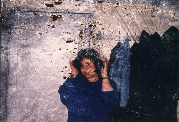 Femme brune souriante en pull bleu avec coiffe en grillage sur la tête. Image avec rayures.