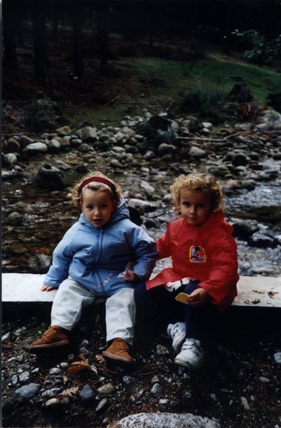 Deux enfants blonds en anorak assis sur un guet au milieu d’un torrent pierreux.