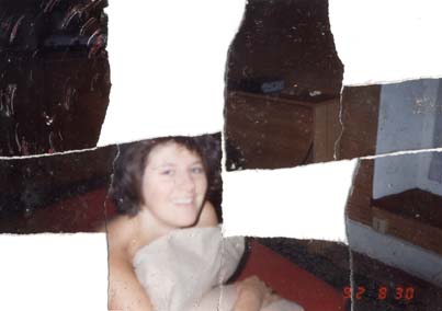 Femme brune souriante sur un lit, les seins cachés par une couverture. Image déchirée, en partie reconstituée.