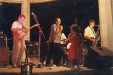 Petite fille sur une scène avec saxophoniste, guitariste, et chanteur.