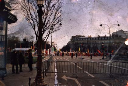 Boulevard parisien avec arbres, lampadaire, manifestants derrière des barrières.