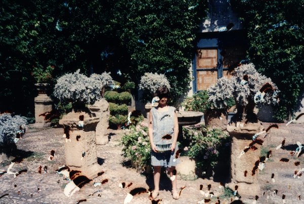 Femme debout dans un jardin avec statues et pots en pierre. Image avec de nombreuses taches.ᴬᴵ