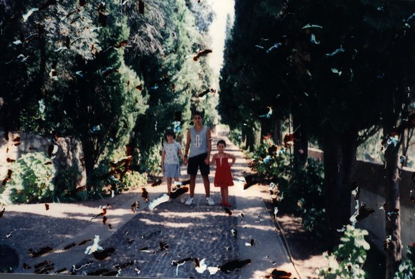 Homme et deux enfants marchant sur une allée bordée d'arbres. Image avec de nombreuses taches.ᴬᴵ