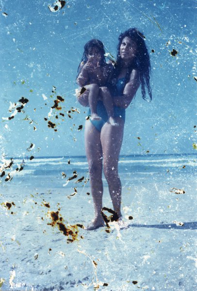 Femme portant un enfant sur une plage. Image très abîmée par des taches.ᴬᴵ