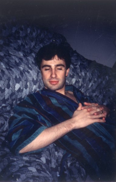 Homme brun en peignoir bleu à rayures allongé les yeux clos sur une couverture.