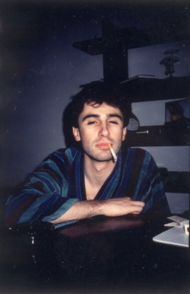 Homme brun en peignoir bleu assis avec une cigarette dans la bouche.