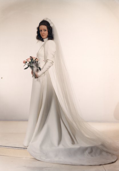 Femme brune pose en robe de mariée avec un bouquet de fleurs.