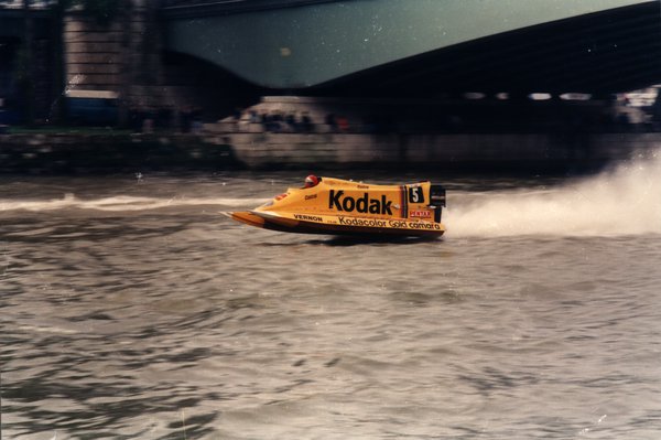 Bateau de course Kodak sous un pont, sillage d'écume.ᴬᴵ