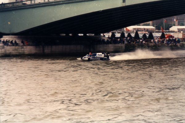 Bateau de course Bricolocation sous un pont, foule sur le quai.ᴬᴵ