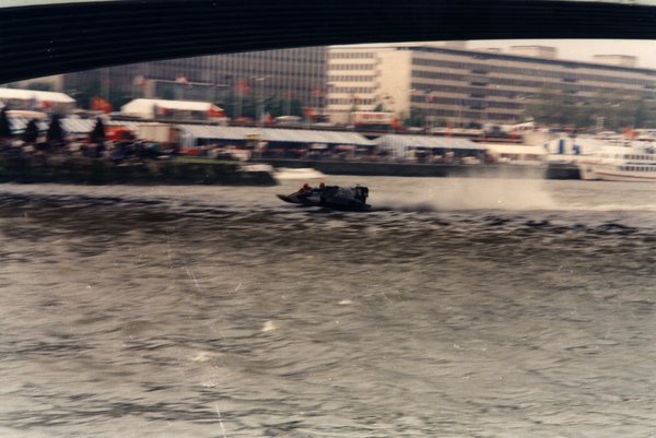 Bateau de course sous un pont, tentes et drapeaux sur le quai.ᴬᴵ