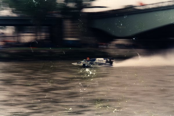 Bateau de course sous un pont, arbres en arrière-plan, effet de mouvement.ᴬᴵ