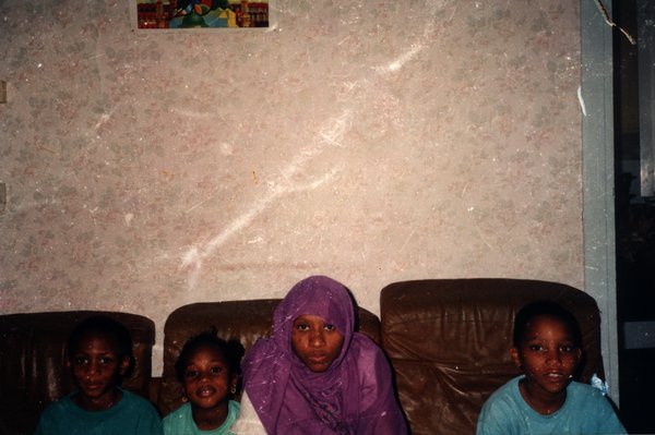 Quatre enfants assis sur un canapé, l'un portant un foulard violet.ᴬᴵ