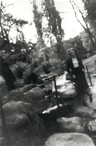 Femme debout au bord d’un chemin dans un bois. Noir et blanc.