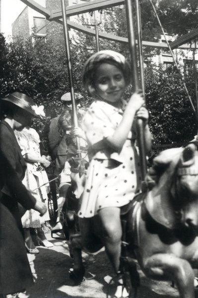 Fillette souriante chevauchant un cheval de bois sur un manège. Noir et blanc.