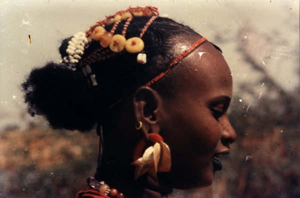 Visage de jeune fille de profil avec une coiffure traditionnelle et divers bijoux.