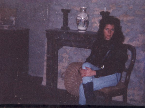 Femme brune en jeans assise sur une chaise devant un manteau de cheminée où est posé un vase.