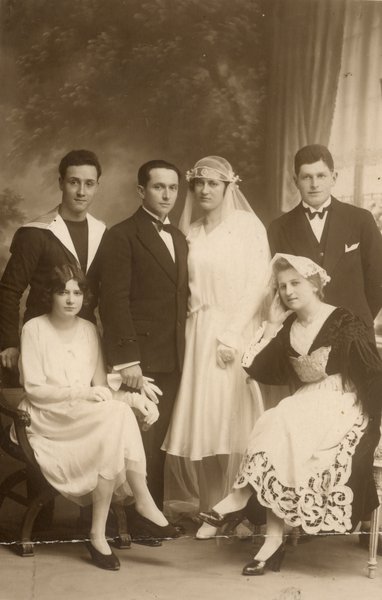 Mariés (1920 ?) entourés d’hommes et de femmes dont l’une est en costume régional. Noir et blanc.